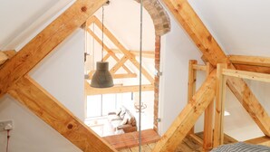 Een kamer met een schuine plafond, houten balken, een hanglamp en uitzicht op een balkon met een bank.