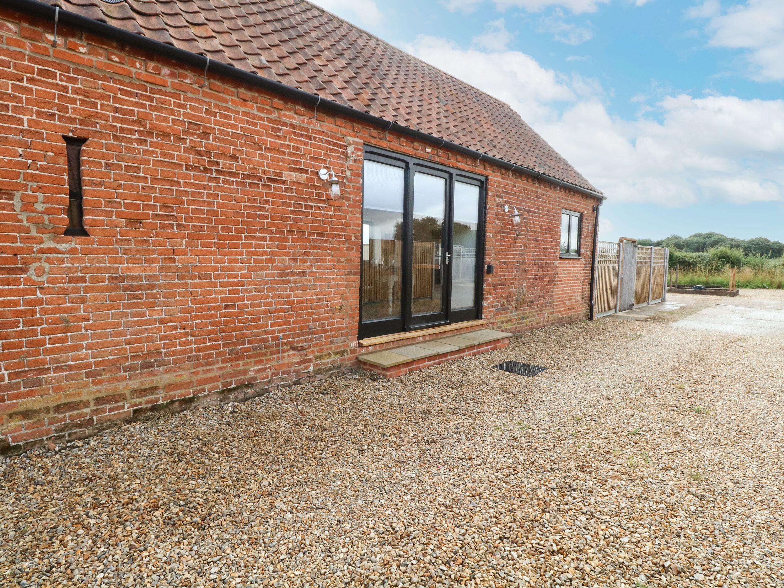 A brick building with a tiled roof, a large glass door, and a gravel driveway.