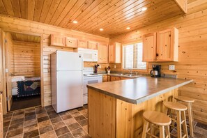 Functional kitchen with wooden cabinetry, refrigerator, microwave, and stove, plus a large island with stools.