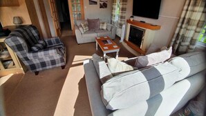 Ein gemütliches Wohnzimmer mit Kamin, einem an der Wand montierten Fernseher und einem Sofa mit kariertem Bezug.
