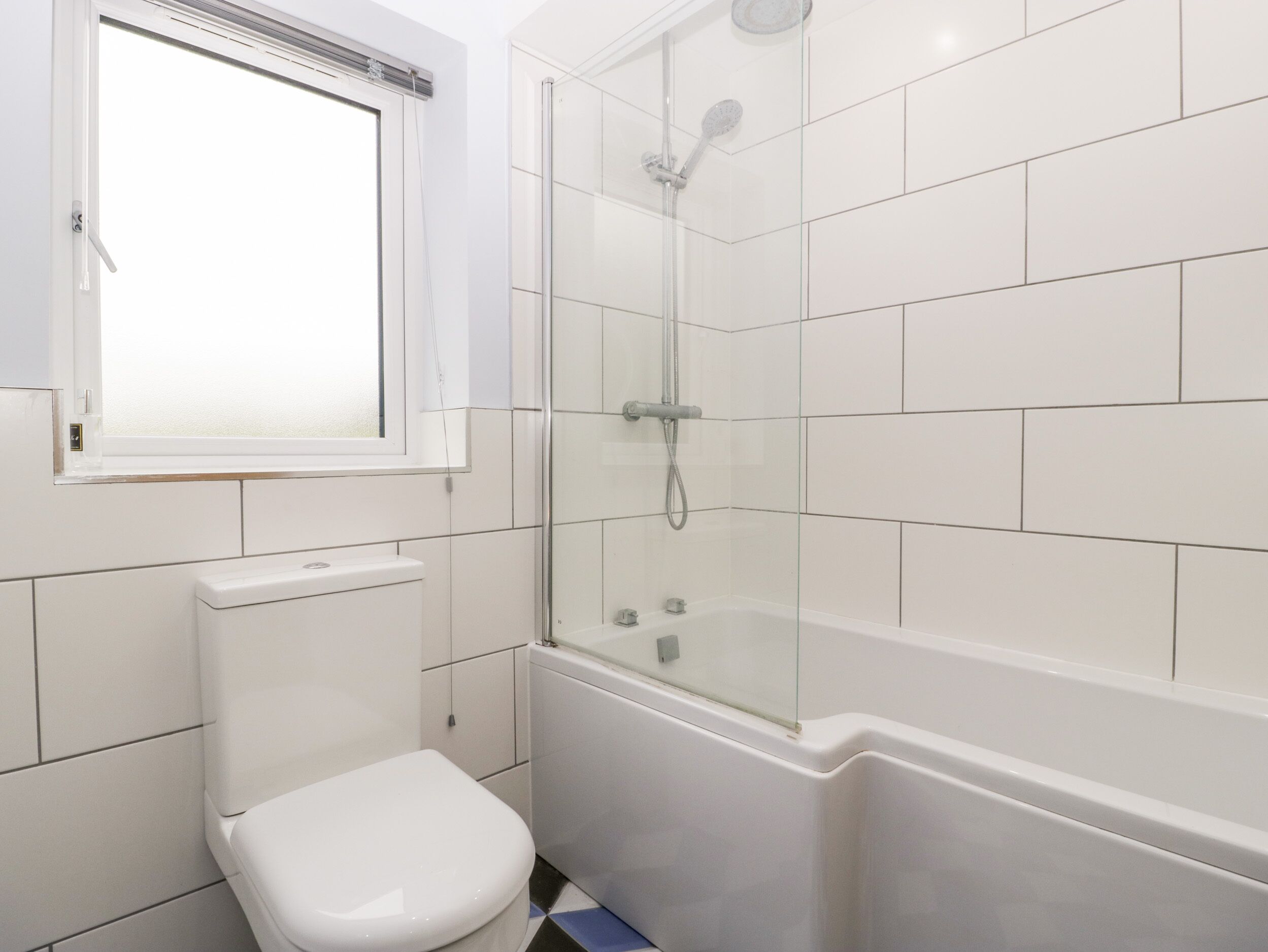 Et badeværelse med toilet, bruseniche i glas og badekar.