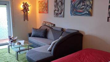 Ein modernes Wohnzimmer mit einem grauen Sofa, einem roten Bett und abstrakter Wandkunst.