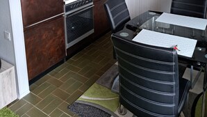A compact kitchen with a refrigerator, stove, and sink. There is a dining table with chairs and a hanging light fixture above.