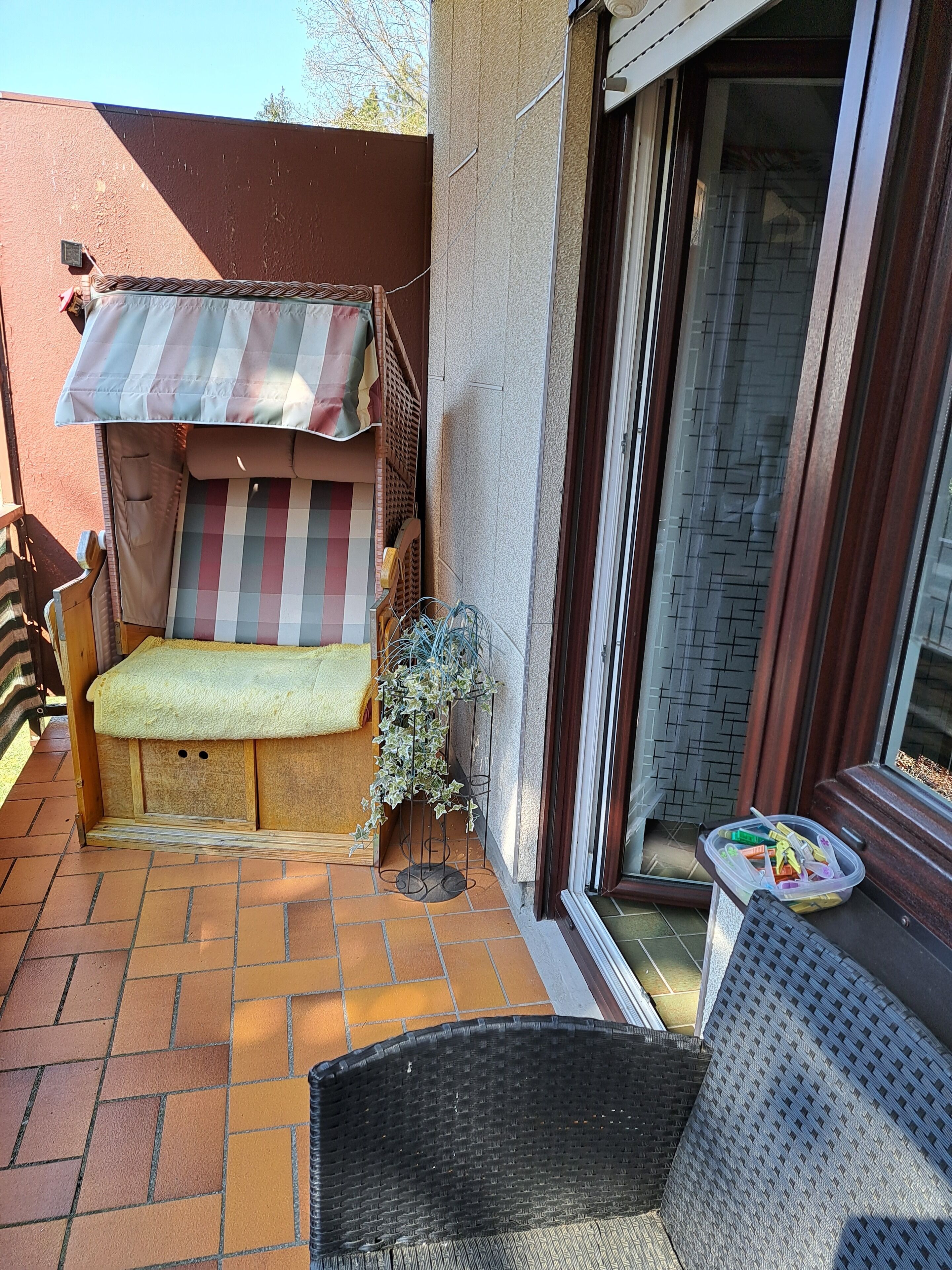 Un petit espace extérieur aménagé avec un banc et une table couverte, un pot de fleurs et une chaise en osier.