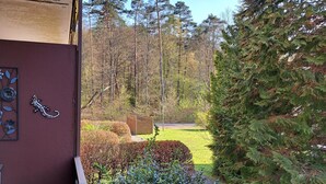 A balcony with a view of a well-maintained garden and tall trees.