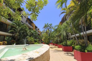 A courtyard with a central fountain, surrounded by lush greenery and palm trees, with multi-story buildings on either side. - Lunada Apartamentos Playa del Carmen (Playa del Carmen)