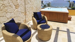 Muebles de mimbre con cojines, una bañera de hidromasaje de madera y un muro de piedra.