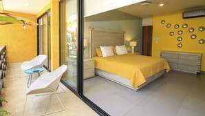Un dormitorio moderno con una cama grande, un ventanal de vidrio a un balcón y una pequeña mesa con sillas.