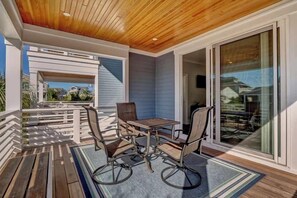 Une terrasse couverte avec un plafond en bois, une table et des chaises, et une vue à travers des portes vitrées.