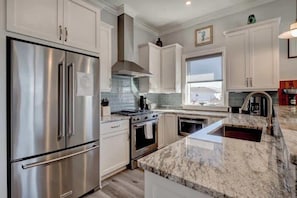 A modern kitchen with stainless steel appliances, white cabinetry, and a marble countertop.