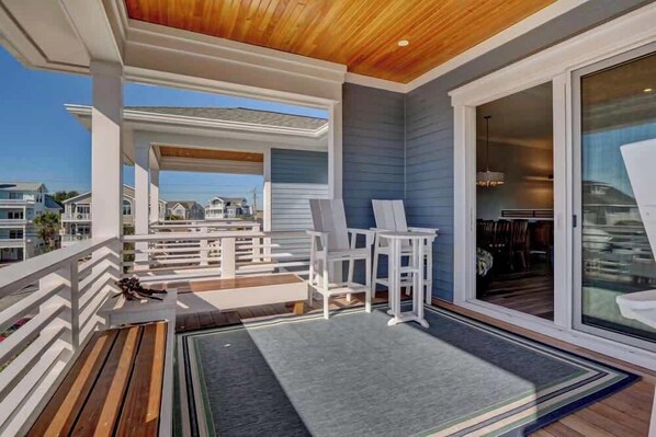 A covered outdoor area with wooden flooring, white furniture, and a view of neighboring houses.