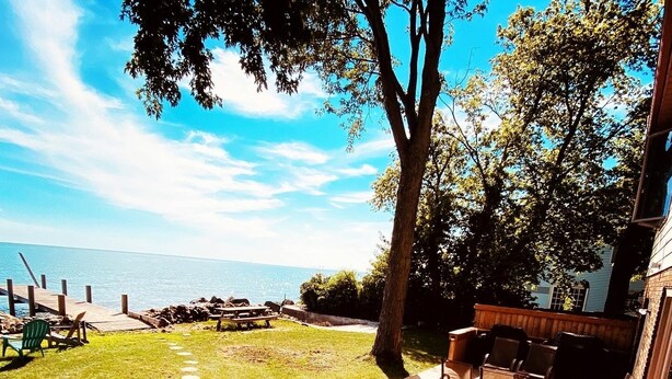 A deck with outdoor furniture, a view of the sea, and a grassy area with stepping stones. - LAKE Escape Retreat - Onsite Beach Dock Waterfront Boat Ramp (Amherstburg)