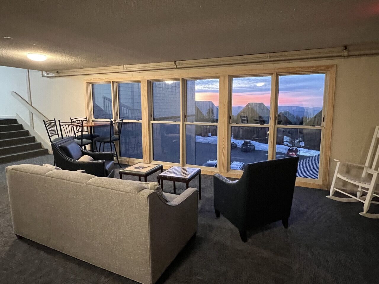 A living room with a sofa, chairs, a small table, and a view of a snowy landscape through large windows.