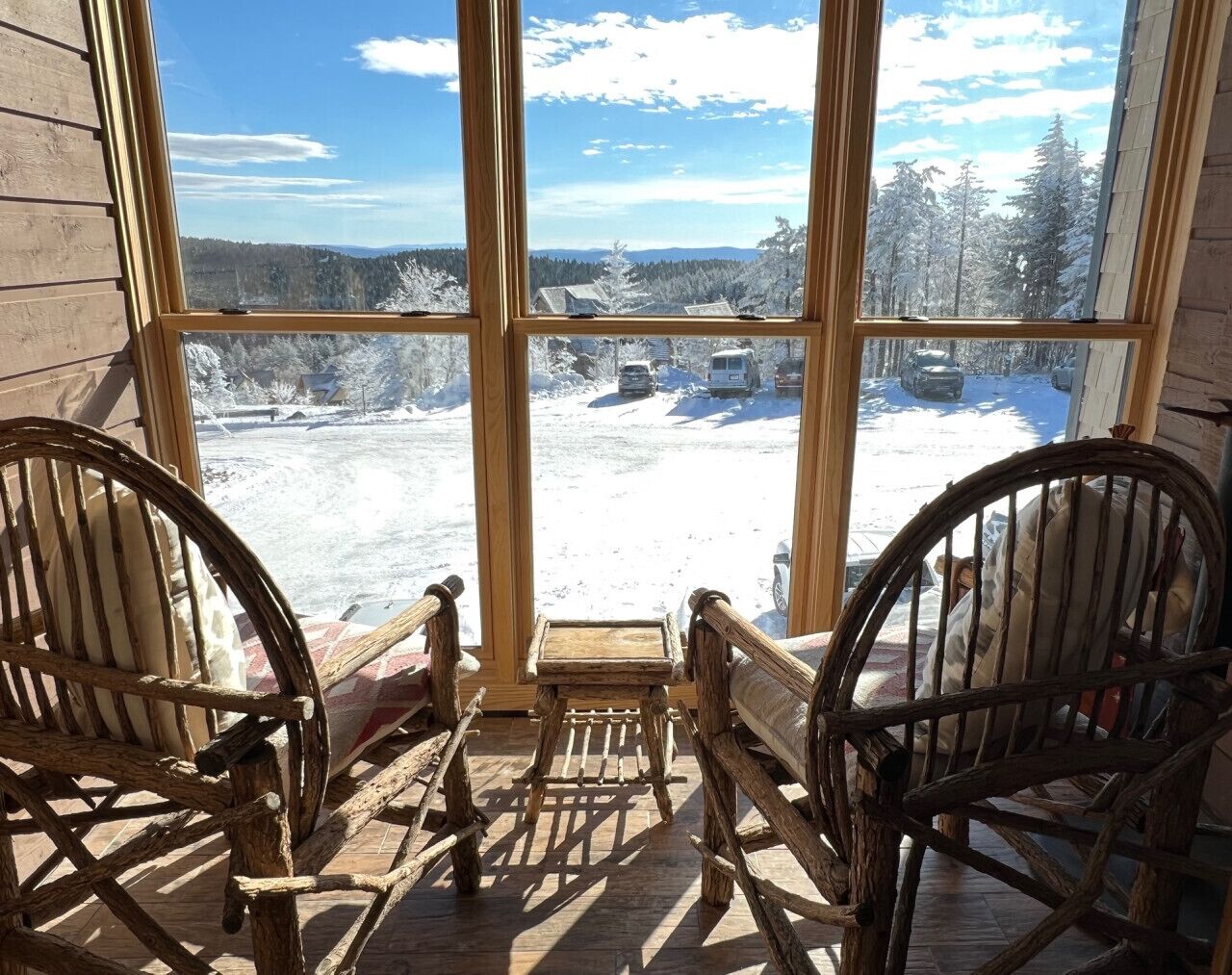 A wooden porch with two rocking chairs facing a snowy landscape through large windows.
