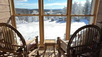 A wooden porch with two rocking chairs facing a snowy landscape through large windows.