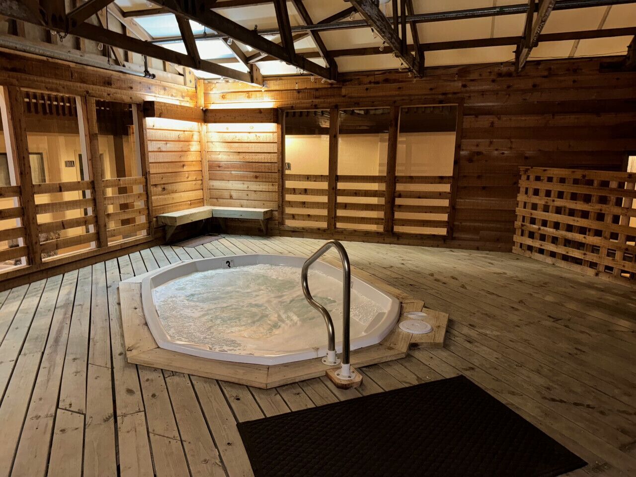 A hot tub in a wooden cabin with a bench and a metal handrail.