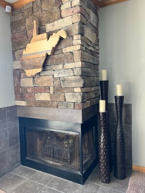 A stone fireplace with a wooden accent piece, two decorative vases, and a metal screen. - Snowshoe Condo 2BR Walking distance to slopes (Snowshoe)