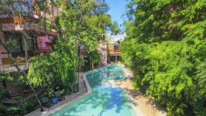 En swimmingpool omgivet af frodig vegetation og en bygning med altaner.