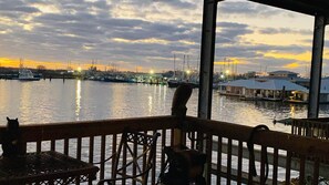 A waterfront view from a covered deck with a railing, overlooking a marina with boats and buildings.