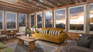A spacious living room with a yellow sofa, a wooden coffee table, and large windows offering a view of the countryside. - Westaway House in Trelights near Port Isaac (Port Isaac)