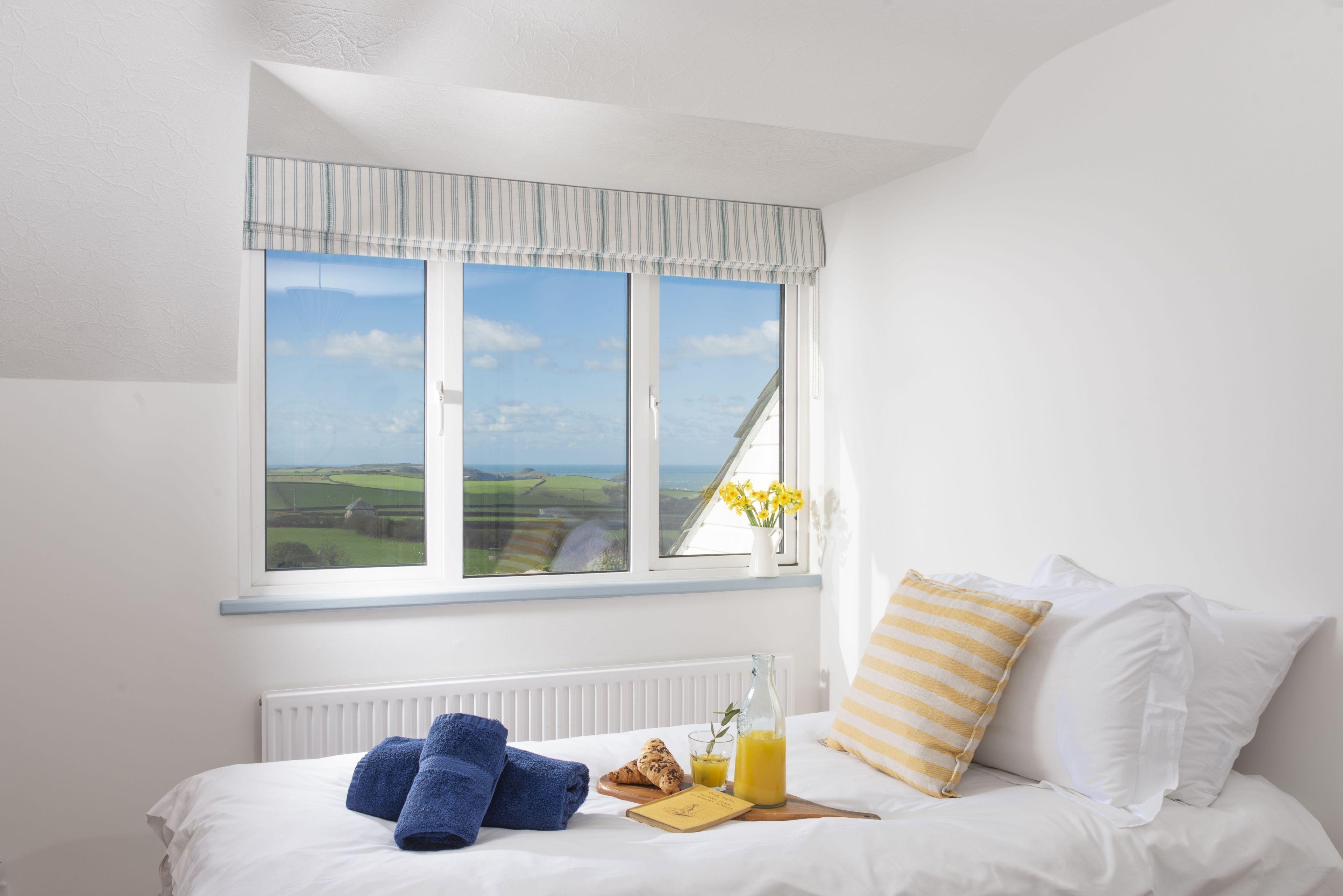 Ein ordentlich bezogenes Bett mit Blick auf die Landschaft durch ein großes Fenster.