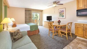 Habitació d'hotel amb un llit, un sofà, una taula de dinar amb cadires, una televisió i armaris de fusta.