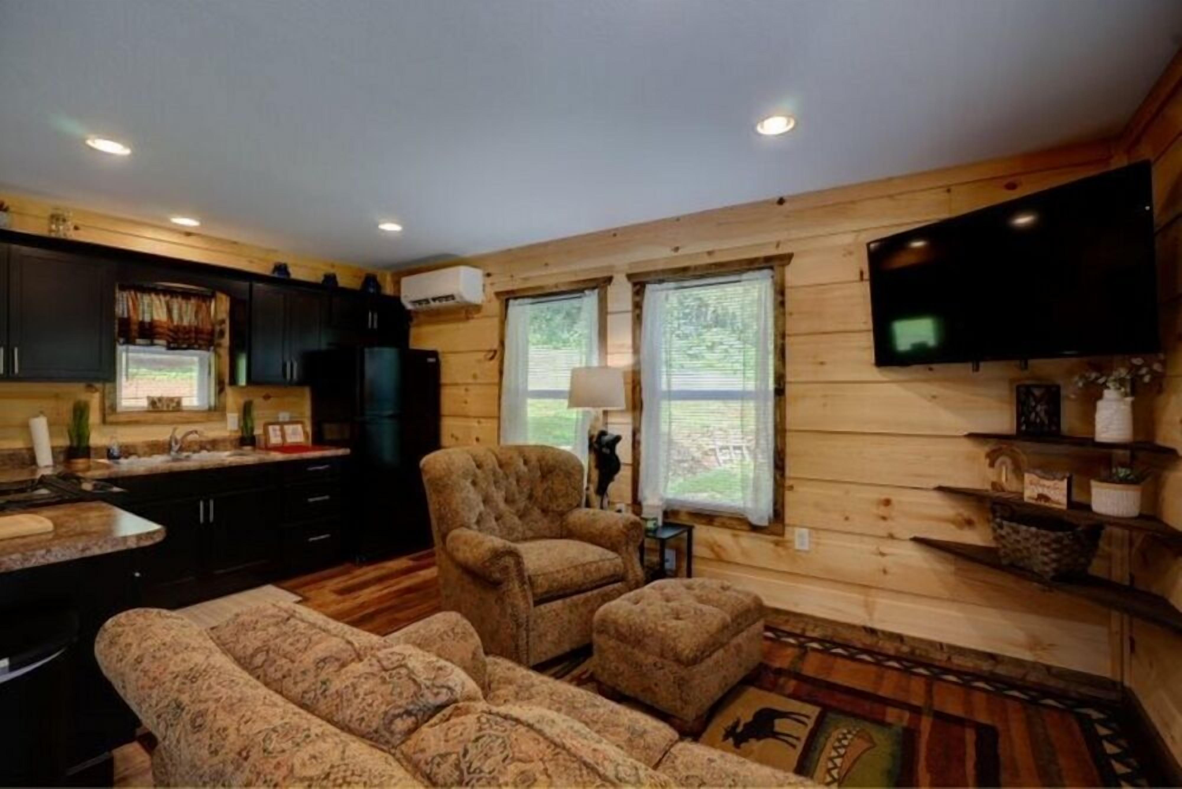 A cozy cabin interior with a wooden interior, a sofa set, a television mounted on the wall, and a kitchen area.
