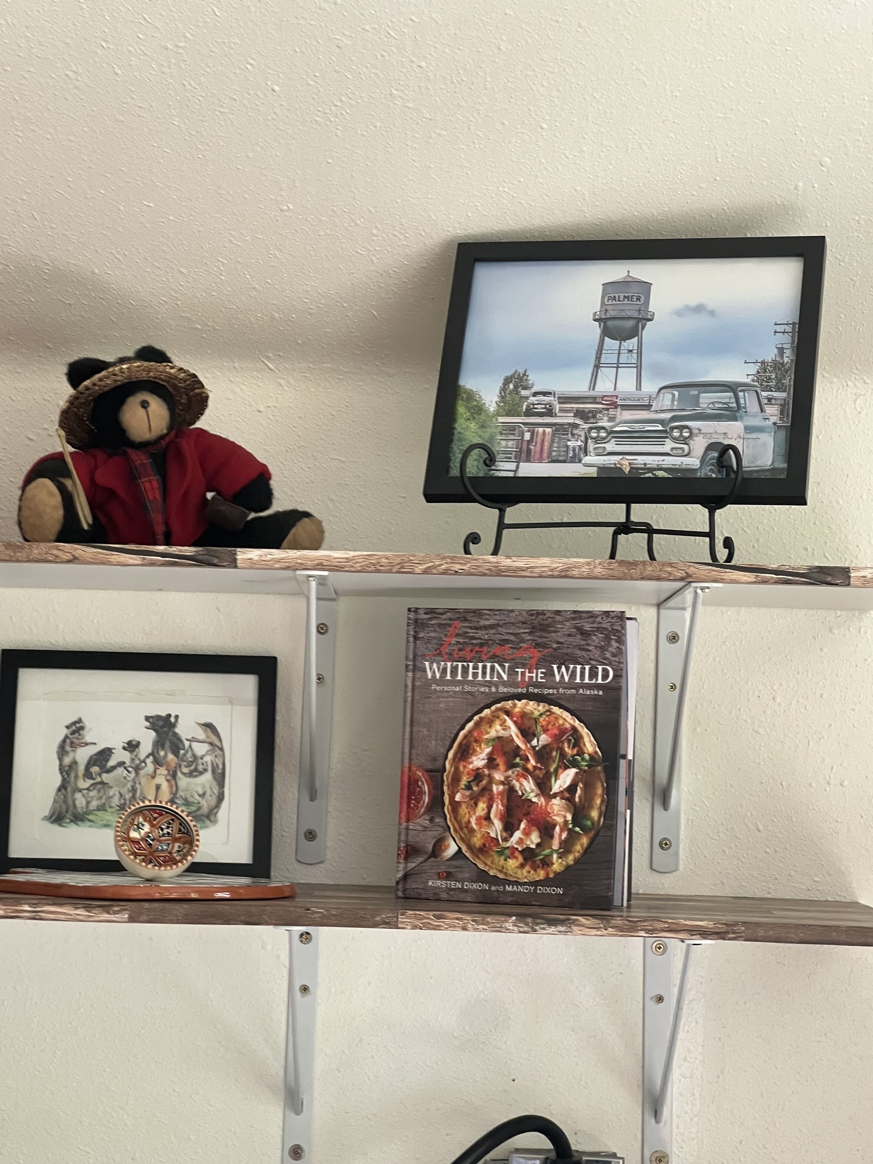 A shelf with a framed picture of a bear, a framed book titled 'Living Within the Wild', and a framed picture of a car.