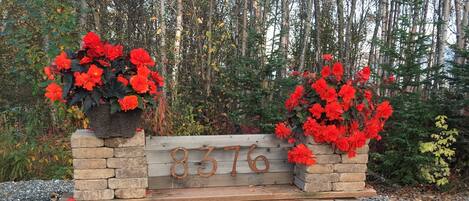 A stone bench with a metal plaque, surrounded by red flowers and a gravel path.