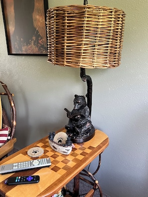 Een tafel met een lamp, een beerbeeldje, een afstandsbediening en een decoratie.