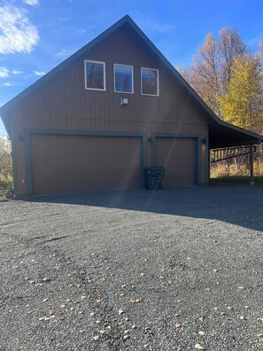 Een gebouw met twee verdiepingen, een garage, een overdekte veranda en een grindpad.