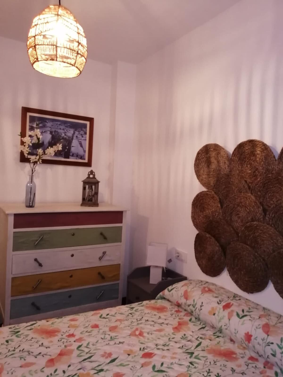 Une chambre à coucher comprenant un lit, une commode, une lampe fixée au mur, un cadre photo et un élément décoratif mural.