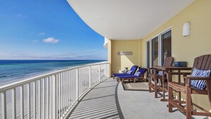Un balcon avec vue sur la plage, deux fauteuils bleus et une table en bois avec des chaises.