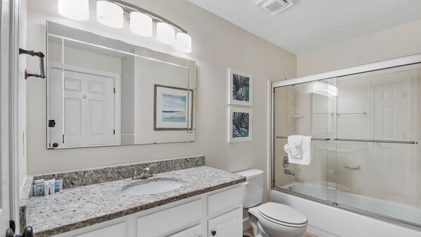 A bathroom with a marble sink, a toilet, a glass shower enclosure, and a mirror with lights.