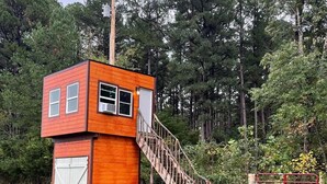 A small wooden cabin with a staircase leading to a loft bedroom, surrounded by a fenced yard and dense trees. - Hollering Pines Retreat-Great for Military, Fugitive Beach, in Mark Twain Forest (Newburg)