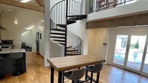 Ein geräumiges Wohnzimmer mit Holzboden, einem Esstisch mit Stühlen, einer modernen Küche und einer Wendeltreppe, die zu einer oberen Ebene führt.