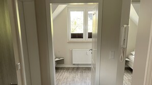 En gang der fører til et soveværelse med et vindue, en radiator og en telefon.