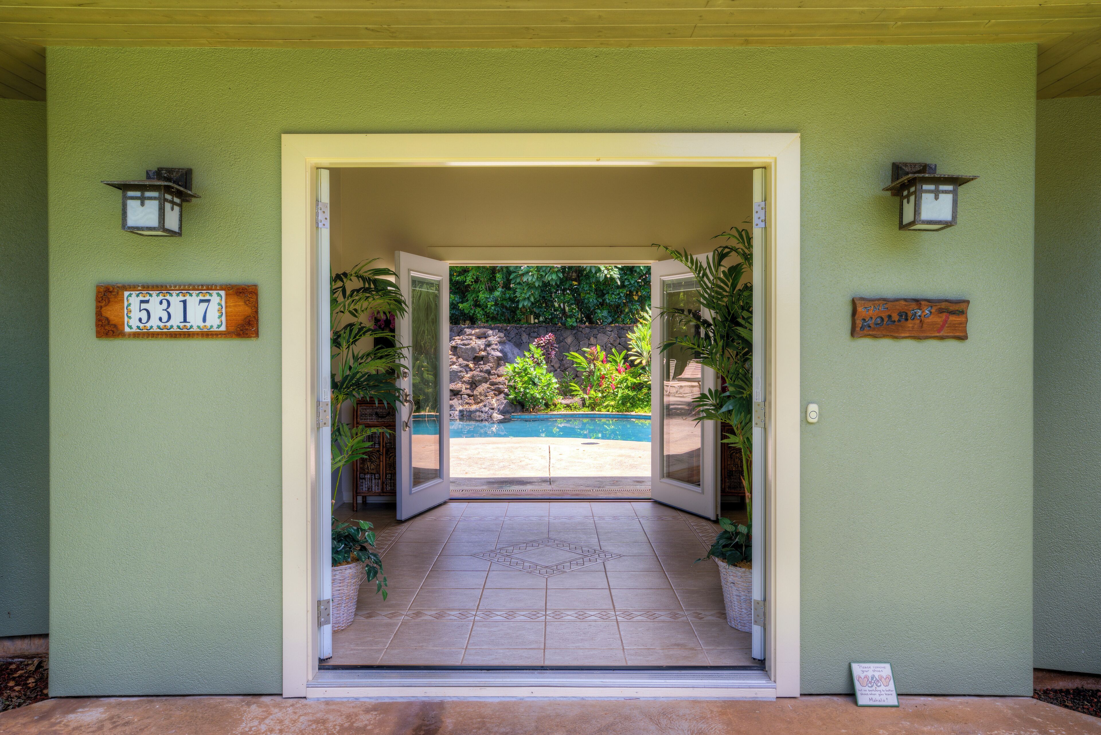 A doorway leading to a pool area with a stone wall and greenery in the background.