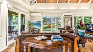 Un salón amplio con techo de madera, ventanas grandes y vistas a un jardín ajardinado.