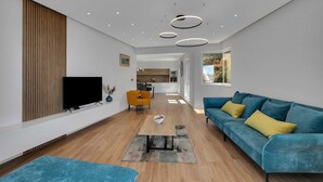 A modern living room with a flat-screen TV, a blue sofa with yellow cushions, a wooden floor, and recessed ceiling lighting. - Villa Seraphine with Pool (Brela)