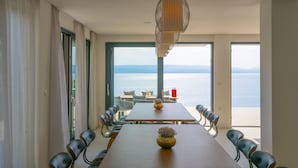 A dining area with a long table, chairs, a vase, and a view of the sea. - Villa Azul Grande with Heated Pool (Brela)