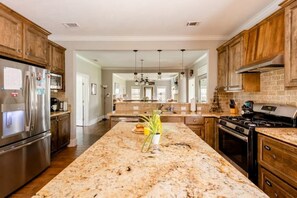 A spacious kitchen with granite countertops, wooden cabinets, stainless steel appliances, and a central island with a plant.
