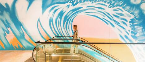 An escalator in a building with a mural of a wave on the wall.