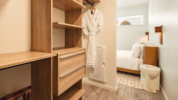 A modern bathroom with a wooden vanity, a white radiator, a toilet, and a bed with white bedding.