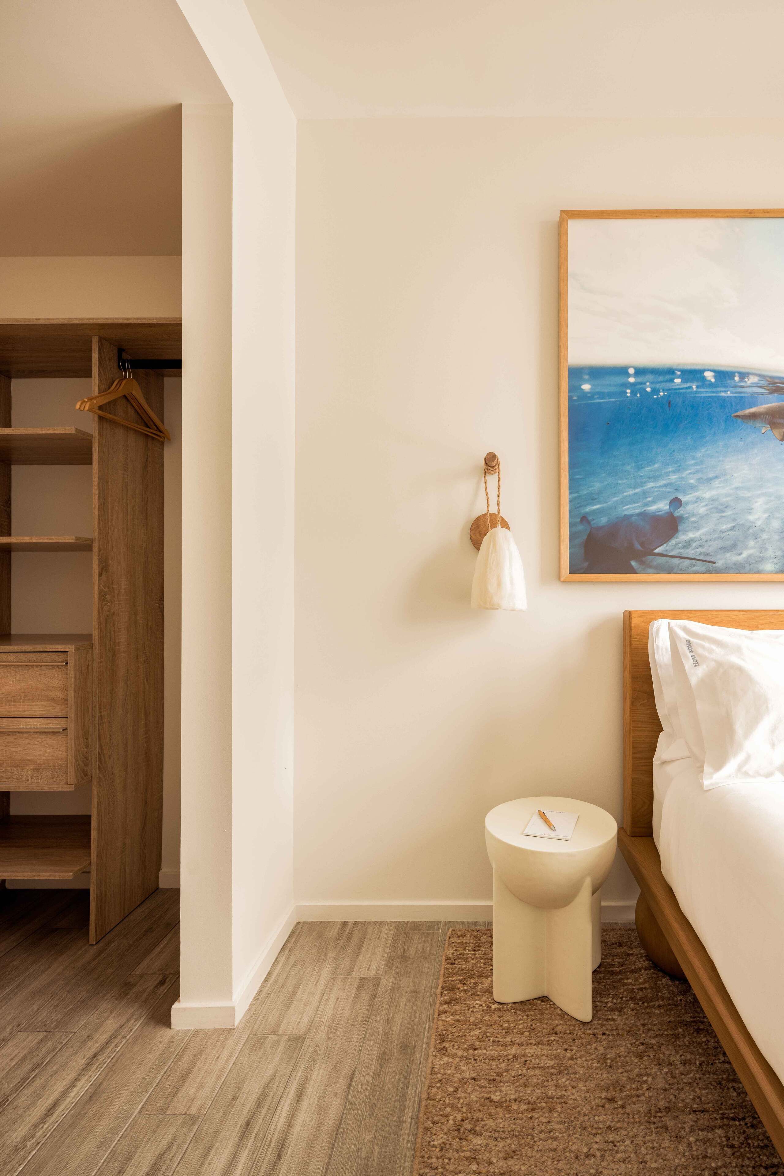Una camera da letto con un letto di legno, un comodino, una lampada sospesa e un quadro raffigurante una spiaggia.