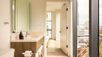 A modern bathroom with a large window, a wooden vanity, and a view of the city.