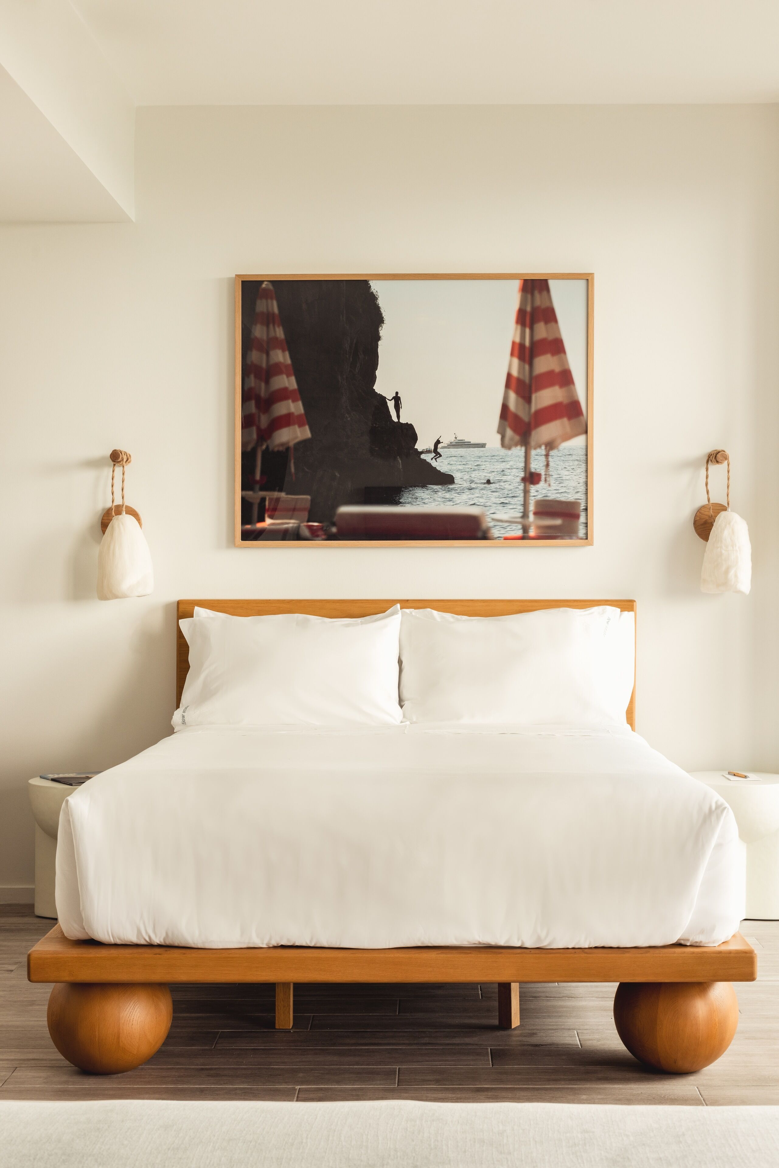 Ein ordentlich bezogenes Bett mit weißen Leinen, einem hölzernen Kopfteil und einem gerahmten Bild einer Strandansicht an der Wand darüber.