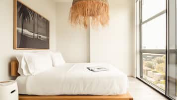 Un dormitorio moderno con una cama grande, una lámpara colgante, un cuadro enmarcado en la pared y vistas de la ciudad a través de un ventanal amplio.