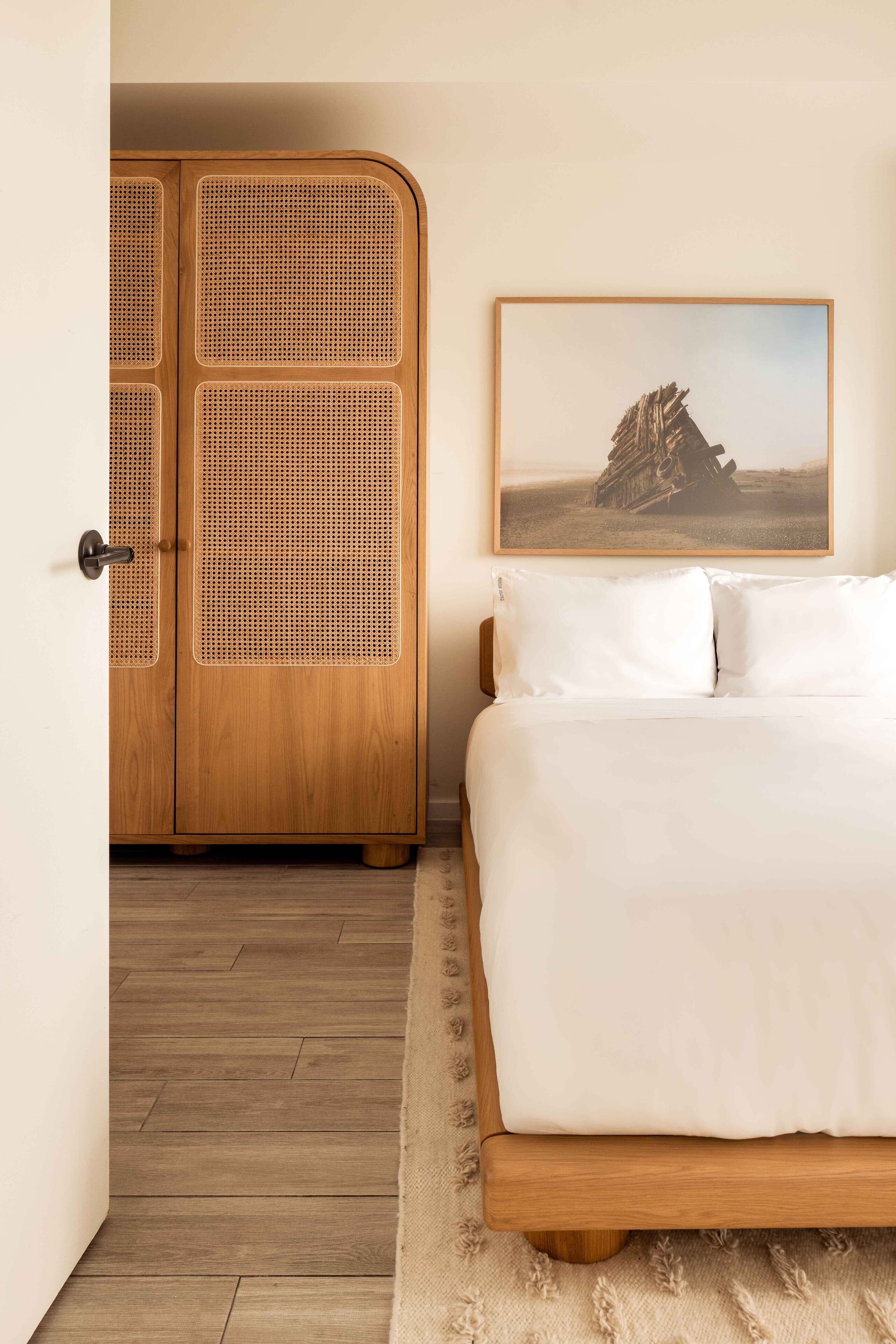 A bedroom with a wooden wardrobe, a bed with white bedding, and a framed picture on the wall.
