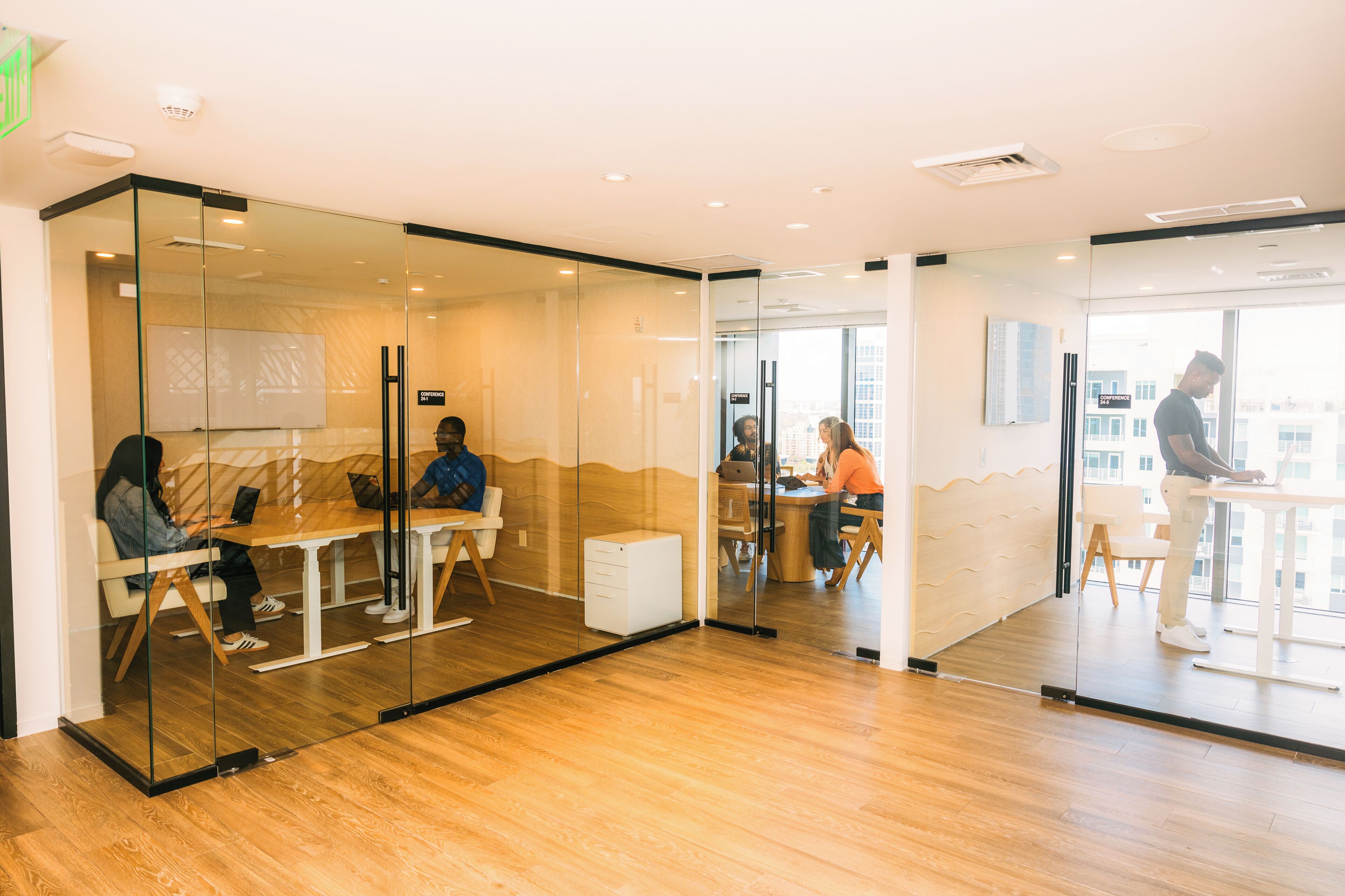 A modern office space with glass partitions, wooden flooring, and a city view.